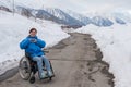 A woman in a wheelchair holds her hands in the shape of a heart in the mountains in winter.