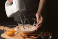 Woman whipping ingredients with mixer at black table, closeup. Cooking delicious eggnog