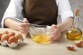 Woman whisking eggs in glass bowl at wooden table, closeup