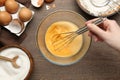 Woman whisking eggs at wooden table, top view