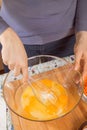 Woman whisks chicken eggs lying in a glass bowl with a kitchen whisk.