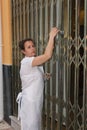 Woman with white apron opening the scissor grill of her business in the morning