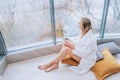 Woman in a white bathrobe enjoying sea view next to big window with cup of coffee. Panoramic window. Floor covering, Vacation Royalty Free Stock Photo