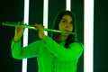Woman in a white blouse plays the flute against a background of bright neon lights. Cute young female artist with a