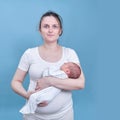 A woman in white clothes is holding a newborn baby on a blue background. Mother with a child boy in her arms, studio shot Royalty Free Stock Photo