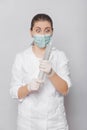 A woman in a white coat, mask and gloves holds a huge syringe in her hands.