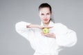 Woman in white coat smiling holding an apple in one hand and leaning against her face with the other Royalty Free Stock Photo