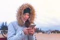 Woman in a white down jacket sitting on a bench on the beach and typing a message on mobile phone. Royalty Free Stock Photo