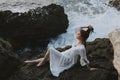 A woman in a white dress barefoot lies on a stone hold by her hair