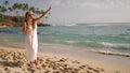 Woman in white dress enjoys ice cream cone on tropical beach. Leisure stroll, sunglasses, curly hair, waves, palms