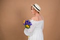 A woman in a white dress and hat stands with her back and holds a bouquet of tulips and irises. March 8. Women's Day. Women's holi