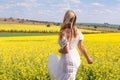 Woman in white dress looking out over fields of golden canola