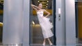 Woman in white dress poses on background of lift. Action. Elegant young woman poses inside modern building. Beautiful