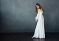 Woman in white dress posing on a dark background barefoot in full growth Royalty Free Stock Photo