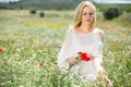 Woman in white dress posing in fields with daisies flowers and holding poppies