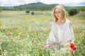 Woman in white dress posing in fields with daisies flowers and holding poppies