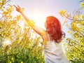 Woman in white dress standing back with raised hands in yellow flowers field