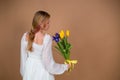 A woman in a white dress stands with her back and holds a bouquet of tulips and irises. March 8. Women's Day. Women's holiday. Mom