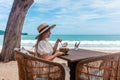 Woman in White Dress and Straw Hat Sitting on Table in Outdoor Beach Cafe Royalty Free Stock Photo