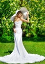 Woman in White Dress and Summer Hat outdoors. Beautiful Bride in Wedding Gown in Spring Blossom Park. Fashion Girl in luxury Royalty Free Stock Photo