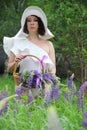 Woman in a white hat with a basket of lilac lupines, vertical photo. A brunette in a white dress and a white hat