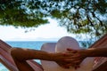 Woman with white hat, lying in the hammock with her hands behind her head, watching the sea Royalty Free Stock Photo