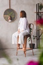 a woman in white on a high chair looks at the reflection in a round mirror.