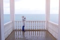 Woman in the white jacket shoots sea waves video on smartphone on beautiful terrace with sea view. Back view. Royalty Free Stock Photo