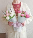 Woman in white knit cardigan holding two bouquets of white and pink tulips, wrapped in white paper. Flowers craft store. Royalty Free Stock Photo