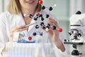 Woman in white lab coat demonstrates model of molecule
