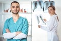 Woman in white lab coat holding at x-ray and man in medical apparel holding.