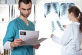 Woman in white lab coat looking at x-ray and man in medical apparel holding ultrasound picture. Royalty Free Stock Photo