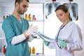 Woman in white lab coat looking at x-ray and man in medical apparel puts on latex glove.