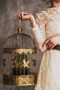 Woman in a white lace dress holding a golden cage with gold birds and a cactus. no face psychology therapy concept