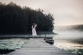 Woman in white light dress run on the pier on foggy morning lake. Royalty Free Stock Photo