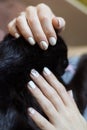 A woman with a white manicure strokes a black cat