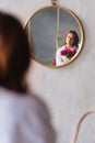 a woman in white with a peonies looks at the reflection in a round mirror.