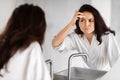 Worried woman checking wrinkles in mirror in bathroom Royalty Free Stock Photo