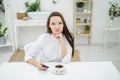 A woman in a white shirt is drinking coffee in a cafe. A female office worker at a lunch break solves a business problem