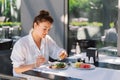 A woman in a white shirt eats lunch or breakfast outdoors in a cafe.