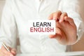 A woman in a white shirt holds a piece of paper with the text: learn english. business concept Royalty Free Stock Photo