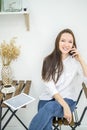A woman in a white shirt and jeans sits in a cafe and drinks coffee. Female office worker at the lunch break talking on