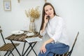 A woman in a white shirt and jeans sits in a cafe with a tablet . Female office worker at the lunch break talking on the