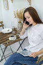 A woman in a white shirt and jeans sits in a cafe with a tablet in her hands. Female office worker at the lunch break