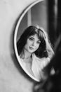 a woman in a white shirt looks at reflection in a round mirror. black and white