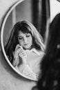 a woman in a white shirt looks at reflection in a round mirror. black and white