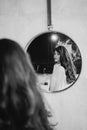 a woman in a white shirt looks at reflection in a round mirror. black and white