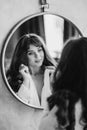 a woman in a white shirt looks at reflection in a round mirror. black and white