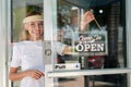 Smiling woman in white shirt wearing face shield hanging open sign for storefront business on the door Royalty Free Stock Photo