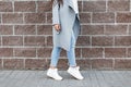 Woman in white sneakers and blue jeans, gray coat near